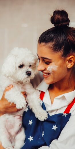 Smiling young woman in the kitchen holding a cute white Maltese dog